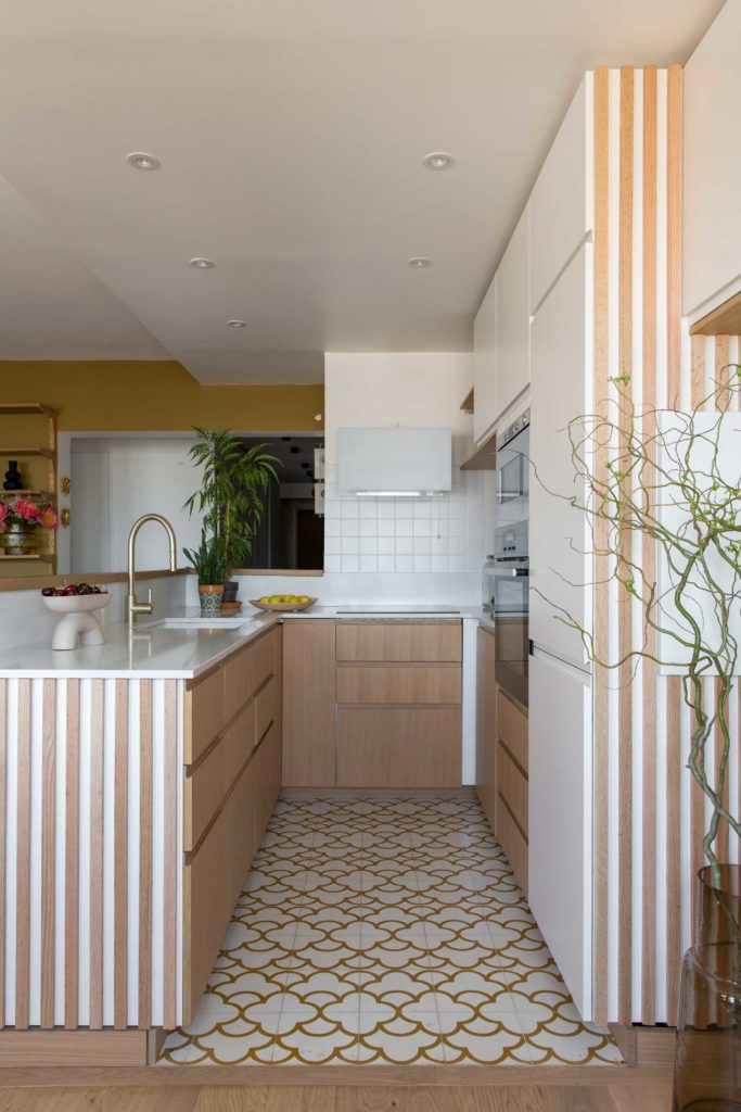 La cuisine de notre projet Jade, plan en U, meubles avec façades en placage chêne, mitigeur en laiton, sol en carreaux de ciment ocre et blanc avec un motif nuage de chez Maison Bahya.
