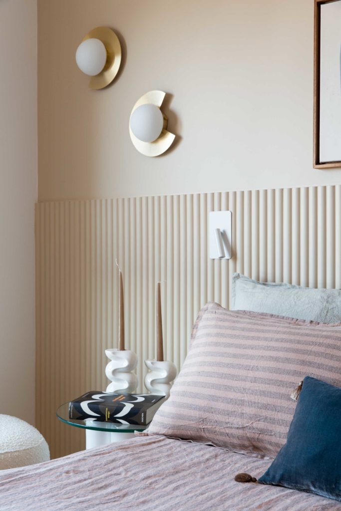Jolie chambre parentale aux couleurs douces, tête de lit en tasseaux arrondis Orac Décor, appliques opaline et laiton, liseuses en metal blanc, guéridon avec bougeoirs en ceramique blanche Cosin. Linge de lit en lin.