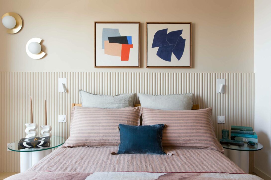 Jolie chambre parentale aux couleurs douces, tête de lit en tasseaux arrondis Orac Décor, appliques opaline et laiton, liseuses en metal balnc, guéridon avec bougeoirs en ceramique blanche Cosin. Linge de lit en lin, tableaux Audrey Noël.