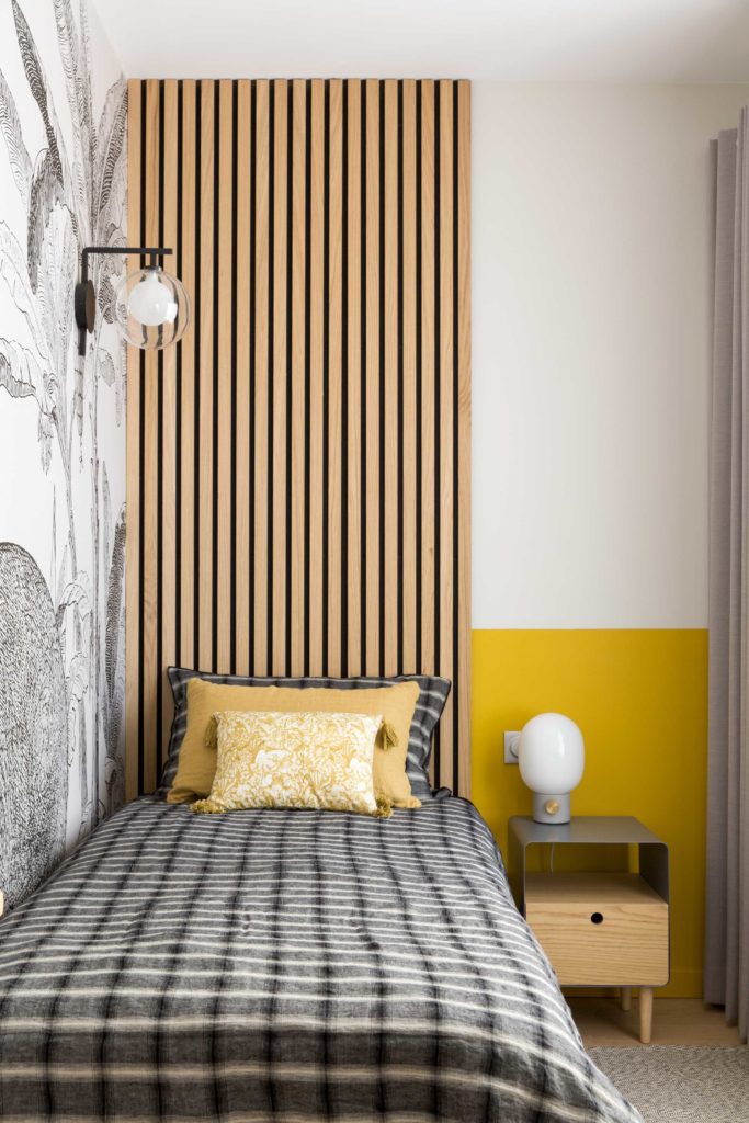Chambre de garçon avec fresque murale, tasseaux en tête de lit peinture peps au mur et petit chevet avec lampe posée.