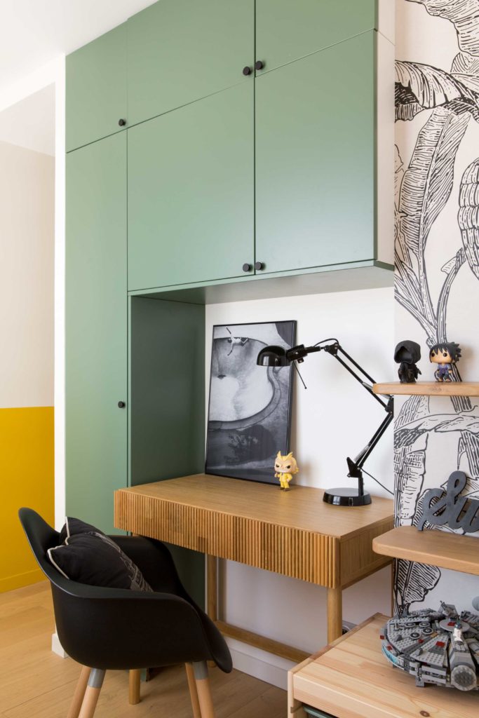Espace bureau de la chambre du jeune garçon, rangements avec façades vertes en laque mate et poignées en metal noir, bureau en chêne et lampe de bureau en metal noir.