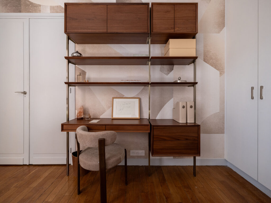 Espace bureau modulable dans la chambre parentale, finition placage noyer et métal brossé, un bureau design et une chaise confortable en tissu beige. Décoration intérieure moderne et fonctionnelle, mettant en valeur des accessoires décoratifs et un papier peint à motifs géométriques doux. Parquet en bois clair et éclairage naturel pour une ambiance chaleureuse et inspirante.